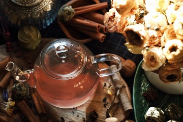 transparent glass teapot with tea, anise, cinnamon, cans and buds and flowers
