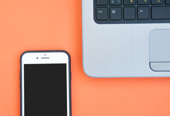 Smartphone and a laptop on an orange background. Top view. Phone in front of a laptop. Homework concept