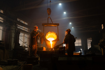 Men filling mold with melted metal in factory