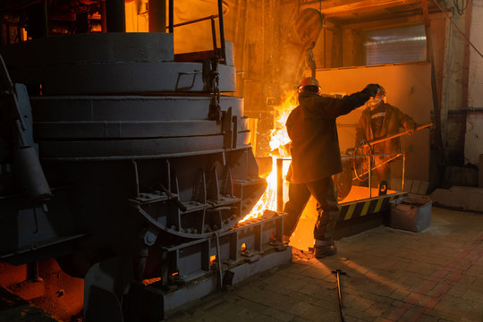 Anonymous men working with hot metal near furnace