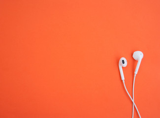 White music earphones on bright orange background. Music concept. Top view