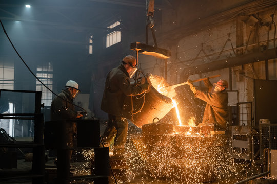Factory workers pouring sparkling metal into mold