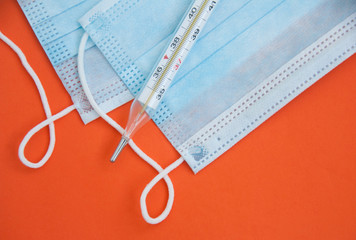 Thermometer and medical masks on an orange background. Close up. Medical concept