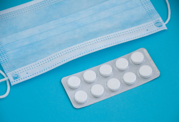 Pills and a medical surgical mask. Blue background. Healthcare concept