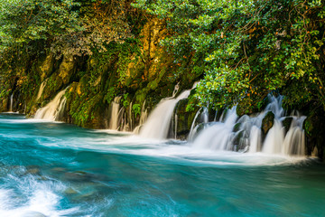 Fototapeta na wymiar Karasu falls blue water current with rocks and green nature around and fence on the left side. Undiscovered beauty of Turey. Travel destination.2020