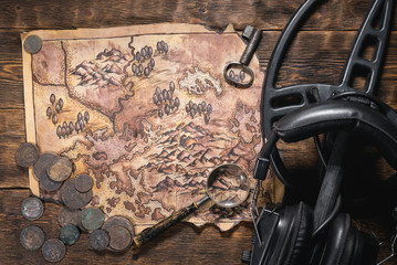 Metal detector, old treasure map and old coins on wooden flat lay table background.