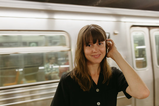 Woman with bangs and brown hair smiling standing near a moving train