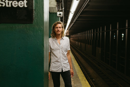 Man with long blonde curly hair waits for a train at a subway stop