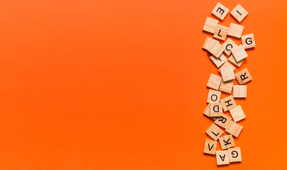 Pile of wooden letters on the surface of a orange paper background, selective focus