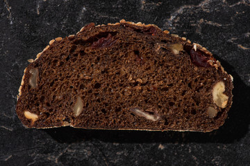 top view of fresh baked black bread slice with nuts on stone black surface