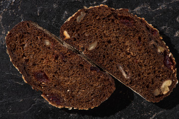 top view of fresh baked black bread slices with nuts on stone black surface