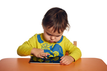 Young child girl is using tablet while sitting at table, isolated over white background