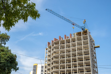 Fototapeta na wymiar Concrete frame of tall apartment building under construction and tower crane in a city.