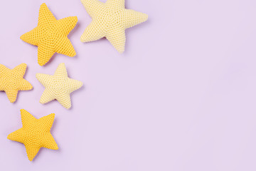 Fototapeta na wymiar Knitted toy yellow stars on purple background. Baby stuff and accessories. Flat lay, top view