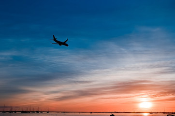 The plane flies to the airport over the river in the city of Faro in Portugal. silhouettes of airplanes and airport, boats in the river, evening city...
