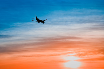 Large plane flies in the evening sunset sky, dramatic painted sky and airplane silhouette with clouds over Lisbon in Portugal.