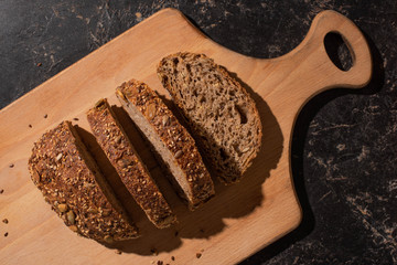 top view of cut whole grain bread on cutting board on stone black surface
