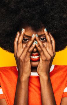 Beautiful Afro Woman posing over yellow background covering her face with hands