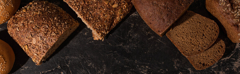 top view of cut whole grain bread on stone black surface, panoramic shot