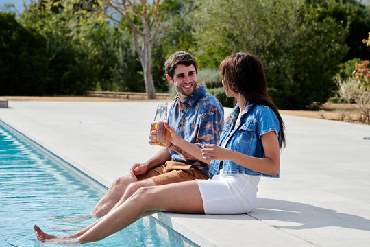 Young couple sitting near swimming pool with legs in water.