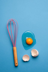 Cracked egg and whisk as a baking concept.