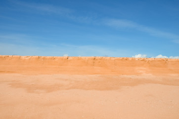 mound of orange sand and dry grass, blue sky with clouds, summer sunny day.