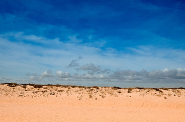 mound of orange sand and dry grass, blue sky with clouds, summer sunny day.