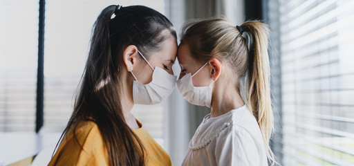 Mother and child with face masks indoors at home, Corona virus and quarantine concept.