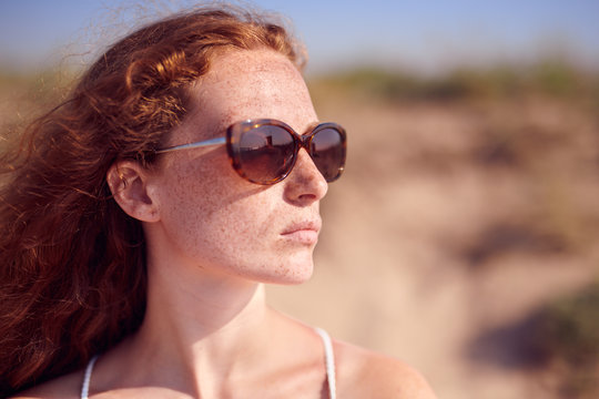Beautiful red haired girl in sunglasses looking at side.
