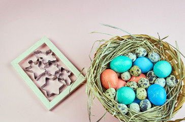 basket in the form of a nest with Easter chicken and quail eggs on a light pink background, a photo frame and cookie shapes inside
