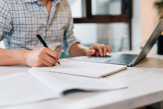 Young Asian man using laptop at home while writing on notebook