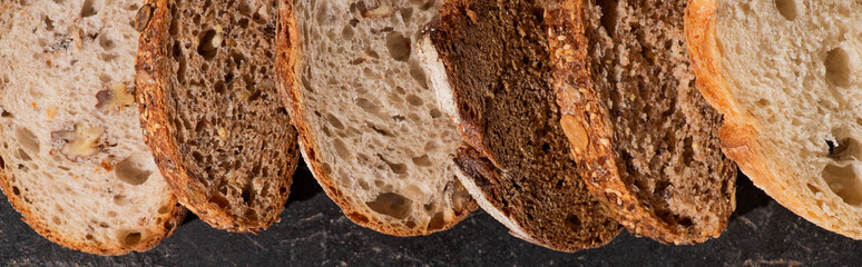 top view of fresh baked bread slices on stone black surface, panoramic shot