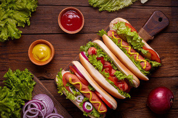 Hot dog with pickles, tomato and lettuce on wooden background. Top view