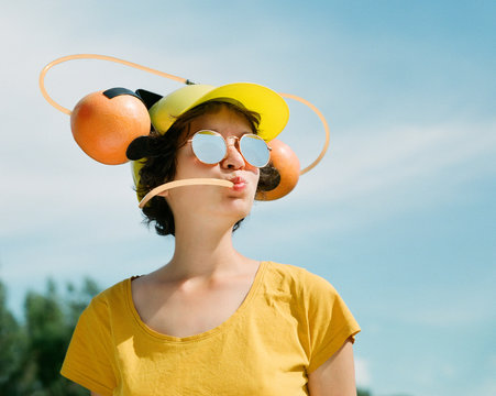 Cheerful girl in sunglasses drinks fresh grapefruit juice via a beer helmet