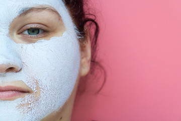 close up face of a beautiful young woman with a cosmetic mask on pink background