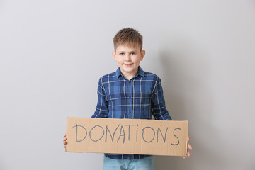 Little boy holding cardboard with text DONATIONS on grey background