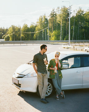 Young couple eating fast food near car.