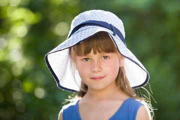 Close-up portrait of happy smiling little girl in a big hat. Child having fun time outdoors in summer.