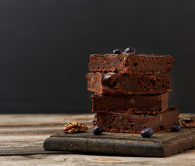 stack of square baked slices of brownie chocolate cake with walnuts on a wooden surface. Cooked homemade food. Chocolate pastry