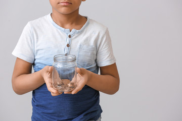 Little African-American boy with jar of coins on grey background. Concept of donations