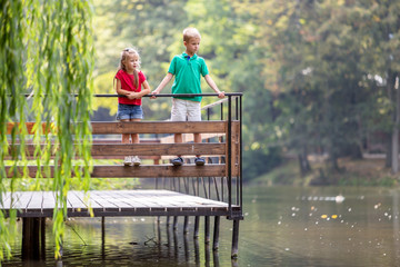 Two children boy and girl standing on wooden deck on a lake shore.