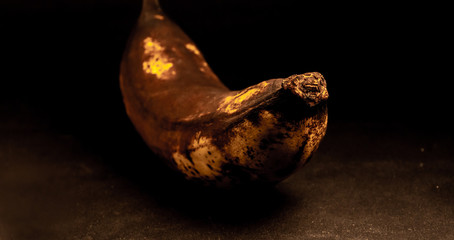 overripe dark skinned banana, lying on the dark table.