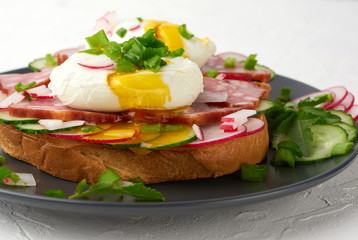 sandwich on toasted white slice of bread with poached eggs, green leaves of arugula, cucumber and radish