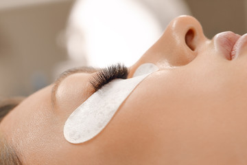 Naklejka premium Eyelashes extensions. Fake eyelashes. Eyelash extension procedure.Close up portrait of woman eye with long eyelashes. Professional stylist lengthening female lashes. Master and client in beauty salon.