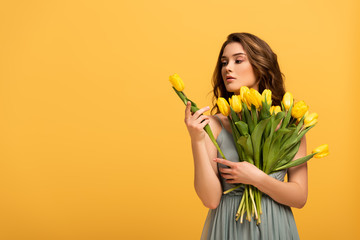 beautiful girl in spring dress holding tulip flowers isolated on yellow