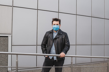 A handsome young businessman in mask on a background of closed office building, coronavirus, illness, infection, quarantine, medical mask