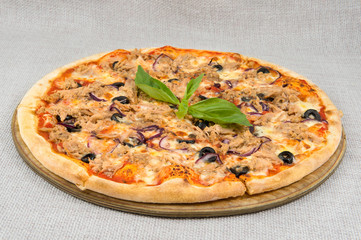 Mushroom pizza with purple onions, black olives, tomato and cheese cut into pieces on a round wooden plate on a gray background