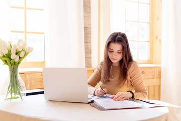 Young girl works with documents and laptop home interior. remote work. quarantined work. telework