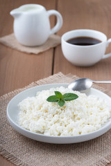  Cottage cheese in a plate, coffee and milk on a wooden table..