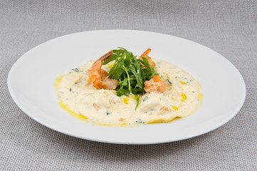 King prawns with green leaves and pasta drenched in milk sauce on a large round white plate on a gray background
